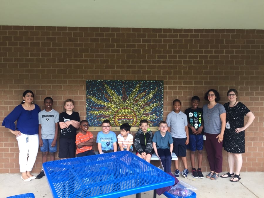 students and teachers in front of a mosaic of the sun
